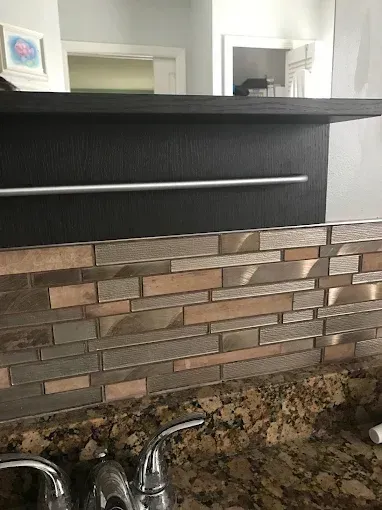 Kitchen backsplash with stacked stone tiles, black counter ledge, and chrome faucet at the bottom.