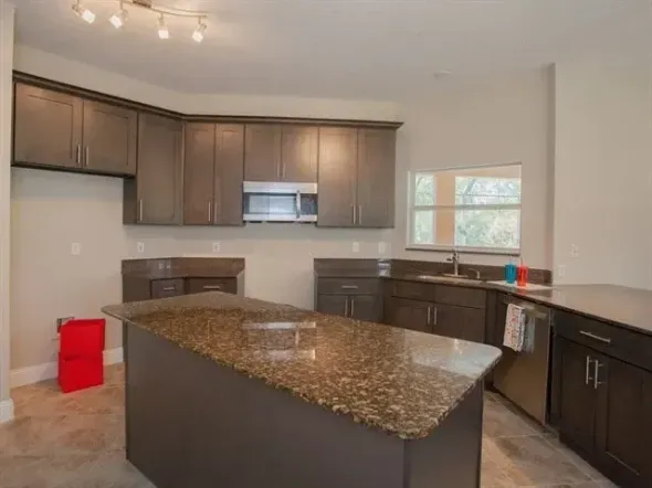 Modern kitchen with dark wood cabinets, granite island, stainless appliances, and a red trash bin