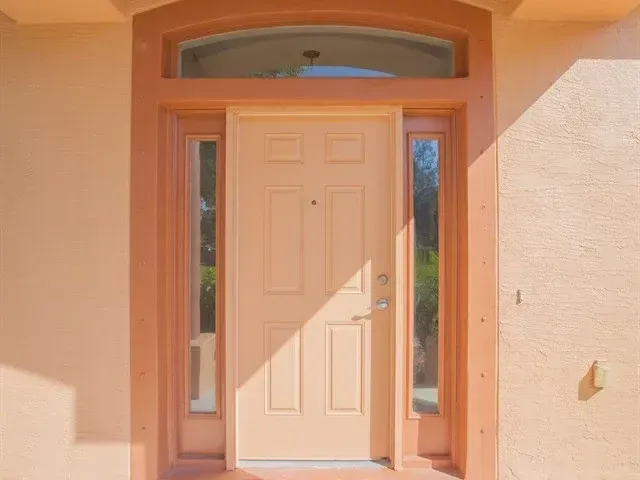 Front entrance with a white door, sidelights, and arched transom in a peach stucco wall.