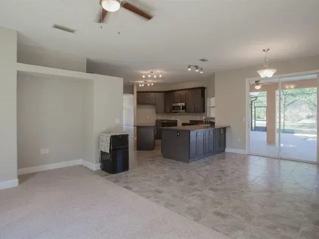 Empty living room and kitchen with tile floor, ceiling fan, and sliding glass doors to a patio.