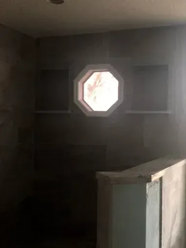 Dim empty room with a small octagonal window and a white cabinet in the foreground.