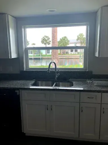 Kitchen sink and window with black countertop, white cabinets, and a view of trees outside