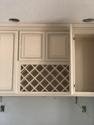 White kitchen cabinets with a wine rack opening and unfinished wall outlets below.