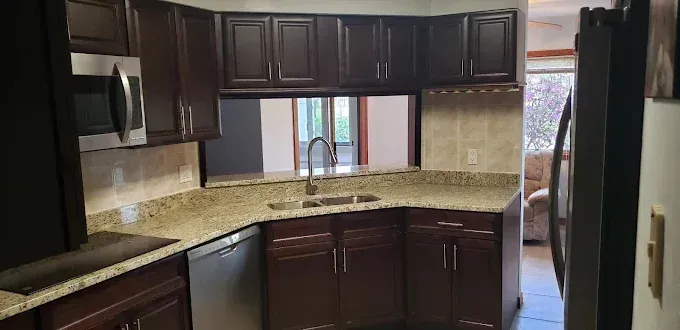 Dark wood kitchen with granite countertops, stainless appliances, and a window over the sink.