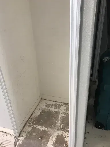 Small white closet corner with a dirty, stained floor and a door frame on the right