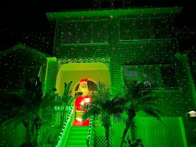 Green-lit house with a Santa decoration by the front steps at night