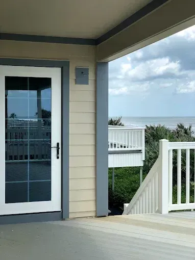 Beachfront porch with white railings, blue door, and ocean view under cloudy sky
