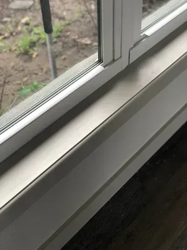 White window frame and sill beside a glass pane, with a view of the outdoors.