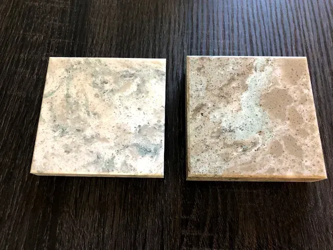 Two small square beige ceramic tiles with mottled gray and brown speckles on a dark wood surface