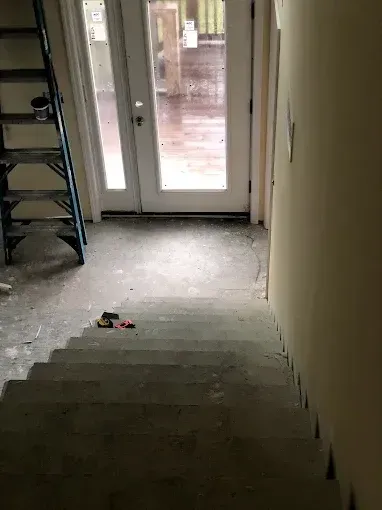 Dim indoor staircase leading to a glass door, with construction debris on the floor.