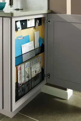Open gray cabinet with mail and magazines stored inside under a countertop.