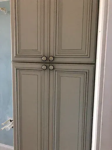 Gray built-in cabinet with paneled doors and round knobs in a room corner.