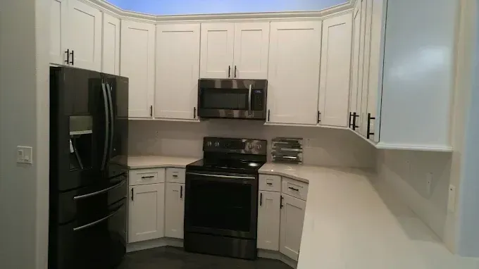 White kitchen with black appliances, beige cabinets, and light countertops.