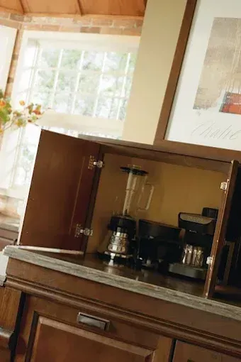 Wooden cabinet nook with a coffee maker and other kitchen appliances beneath framed artwork.