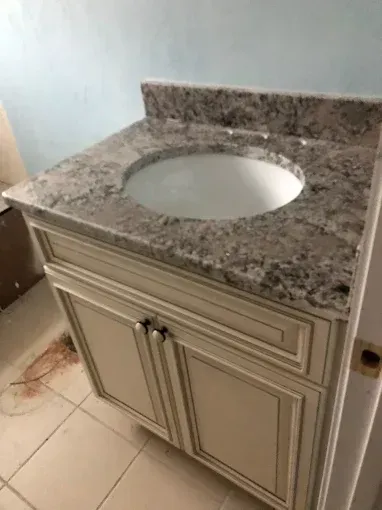 Bathroom vanity with granite countertop and round sink, against a light blue wall