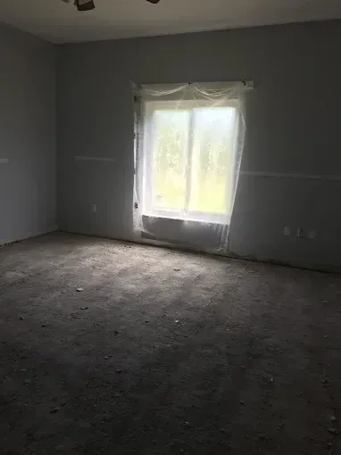 Empty gray room with bare floor and a bright window covered by a sheer curtain