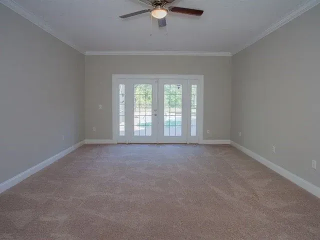Empty carpeted living room with gray walls, ceiling fan, and French doors leading outside