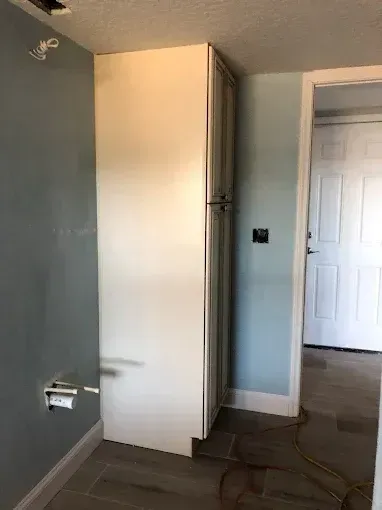 Empty room with blue-gray walls, a tall white cabinet, and a door in the background.