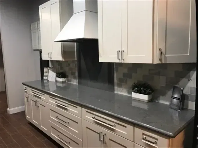 Modern kitchen with white cabinets, gray countertop, stainless range hood, and tiled backsplash.