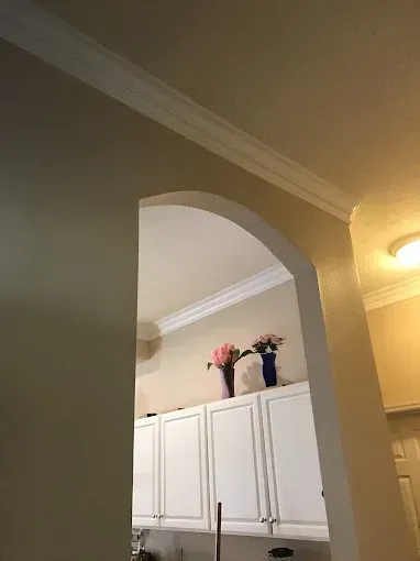 Arched doorway to a kitchen with white cabinets and flowers on top, warm ceiling light nearby