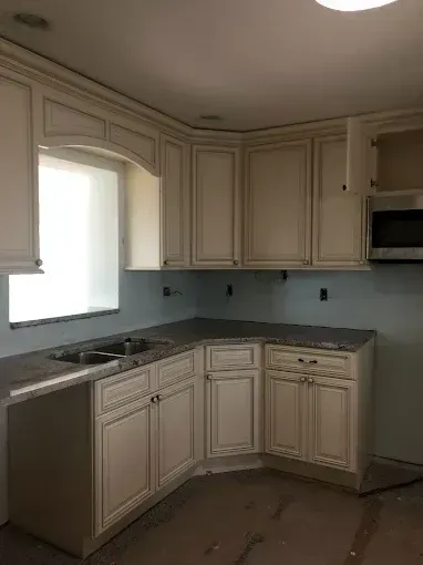Empty kitchen with light-colored cabinets, dark countertop, sink, and window above it.