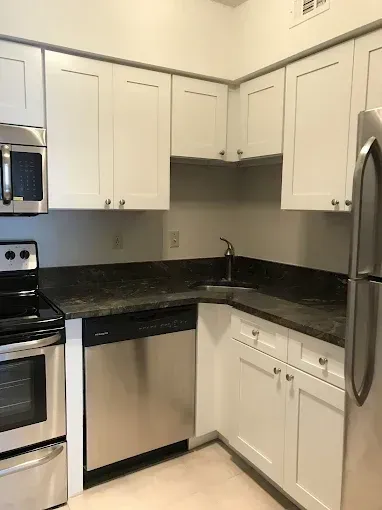 Compact kitchen corner with white cabinets, black countertops, stainless stove and refrigerator
