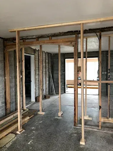 Unfinished interior with exposed framing, temporary wood supports, and a hallway opening to a bright room.