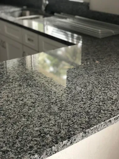 Granite kitchen countertop beside a stainless steel sink and gray cabinets