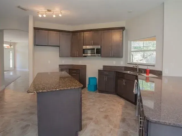 Empty modern kitchen with dark wood cabinets, granite island, and stainless steel appliances
