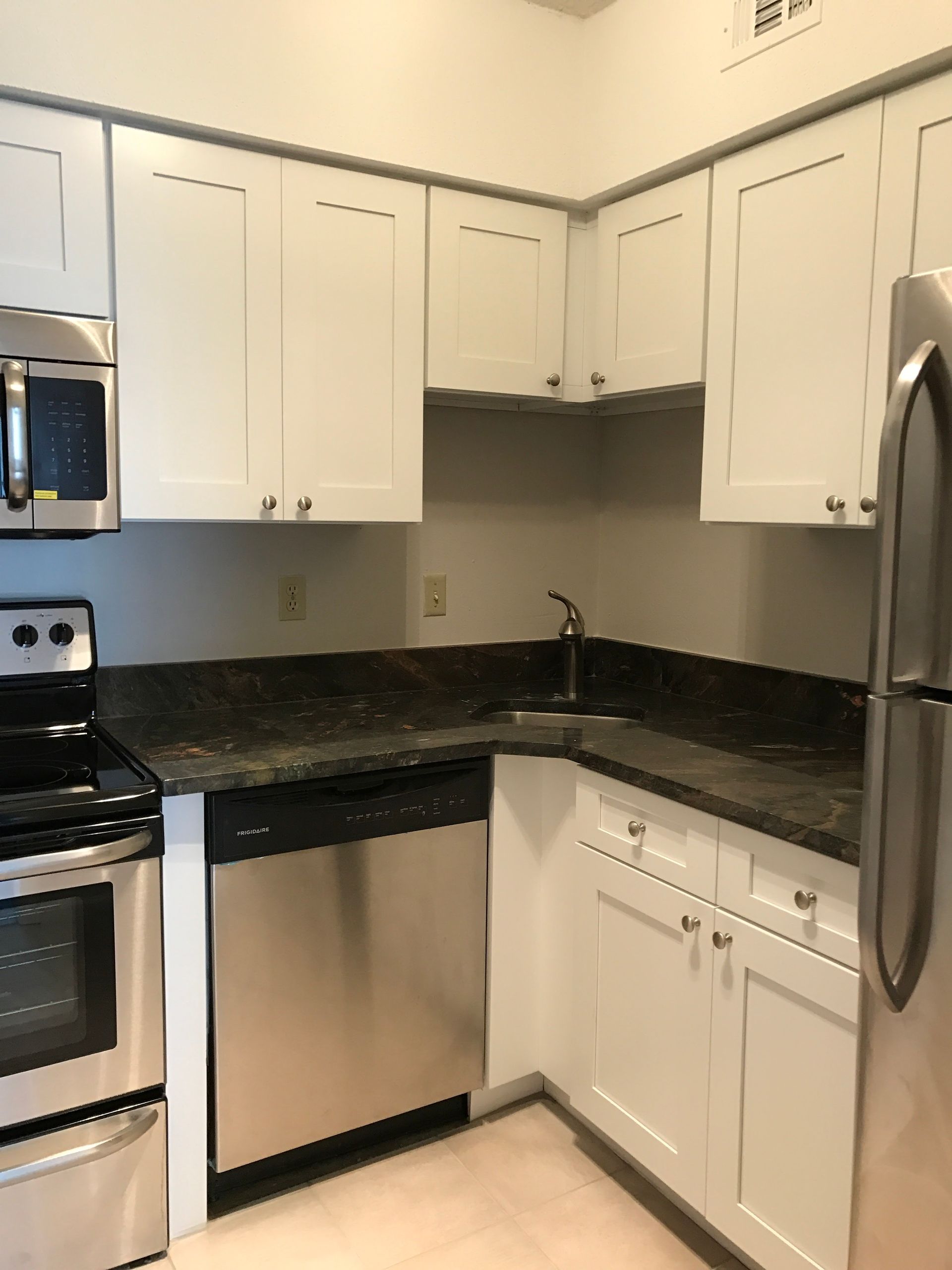 Small kitchen with white cabinets, black countertops, stainless steel appliances, and tiled floor
