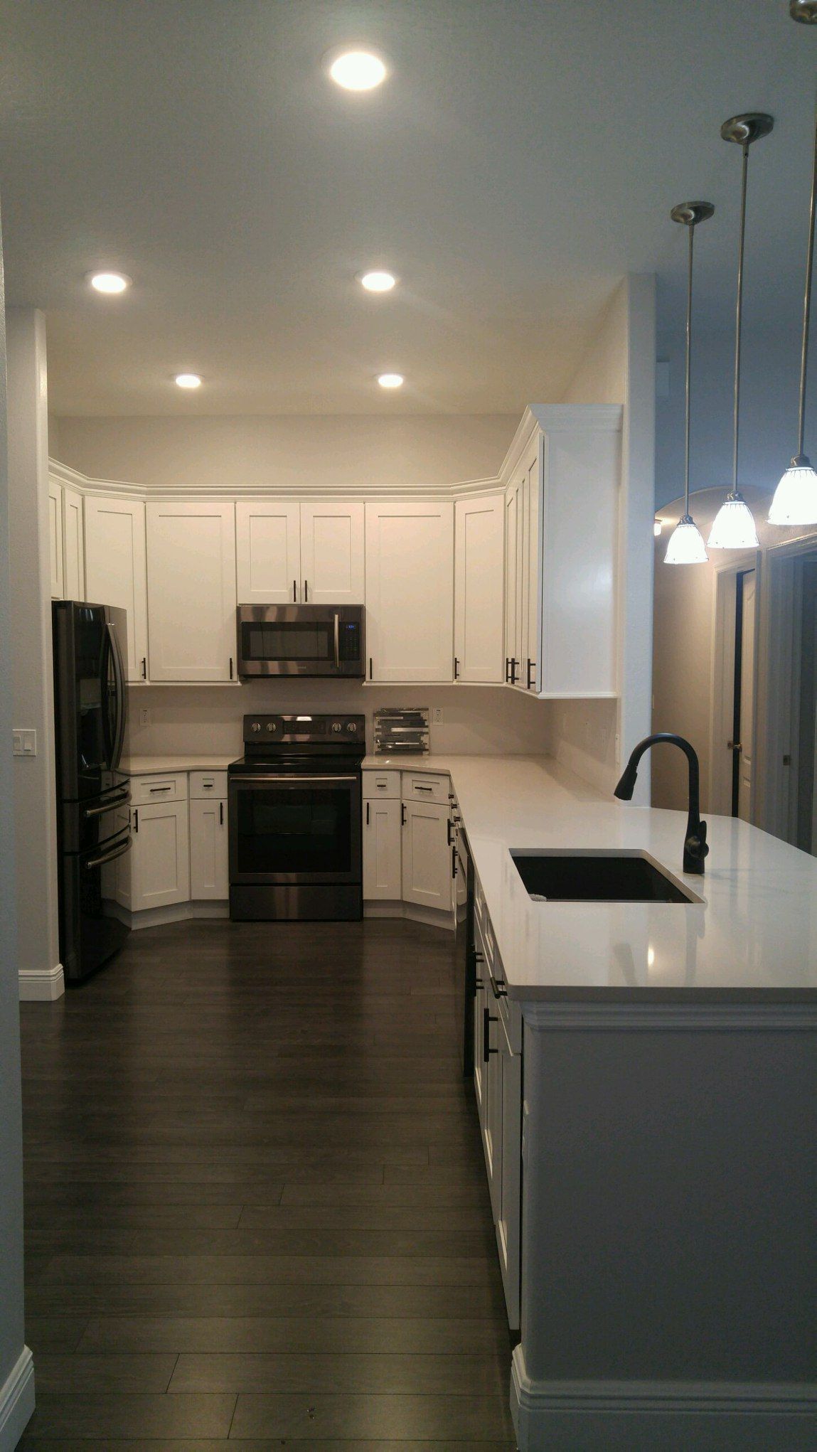 Bright modern kitchen with white cabinets, stainless appliances, dark floors, and pendant lights over the island