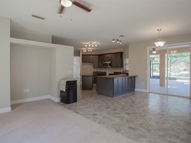 Empty open-plan living room and kitchen with tile floor, ceiling fan, and sliding glass door to patio
