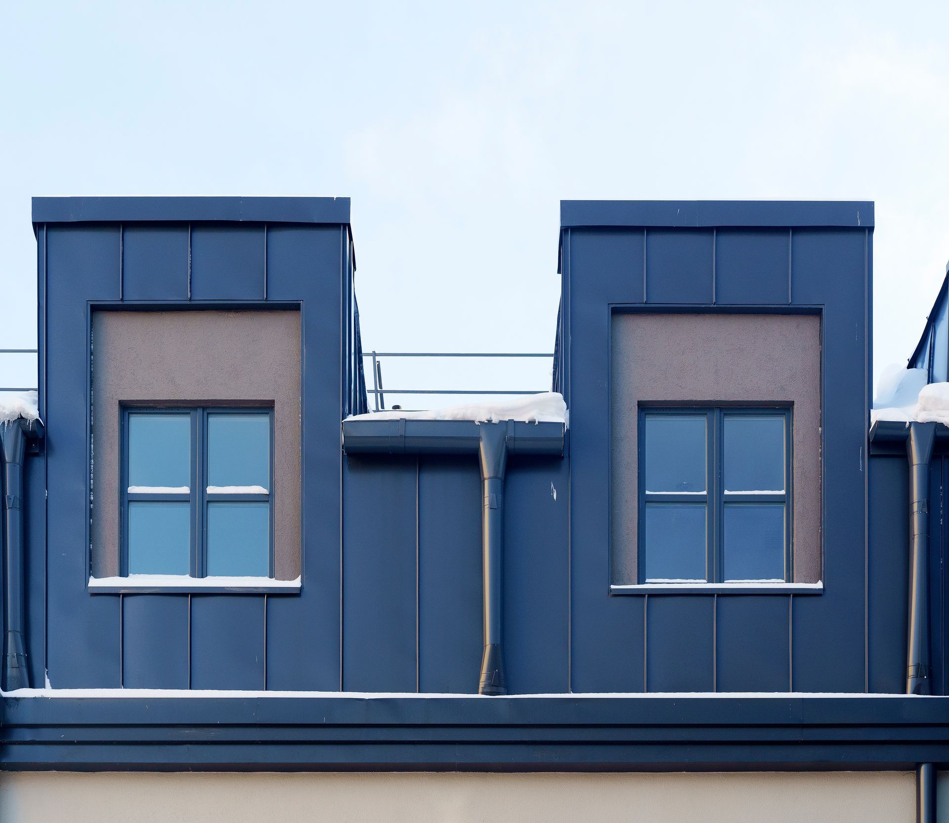 Deux lucarnes bleu foncé avec des panneaux texturés marron, se détachant sur un ciel bleu clair.
