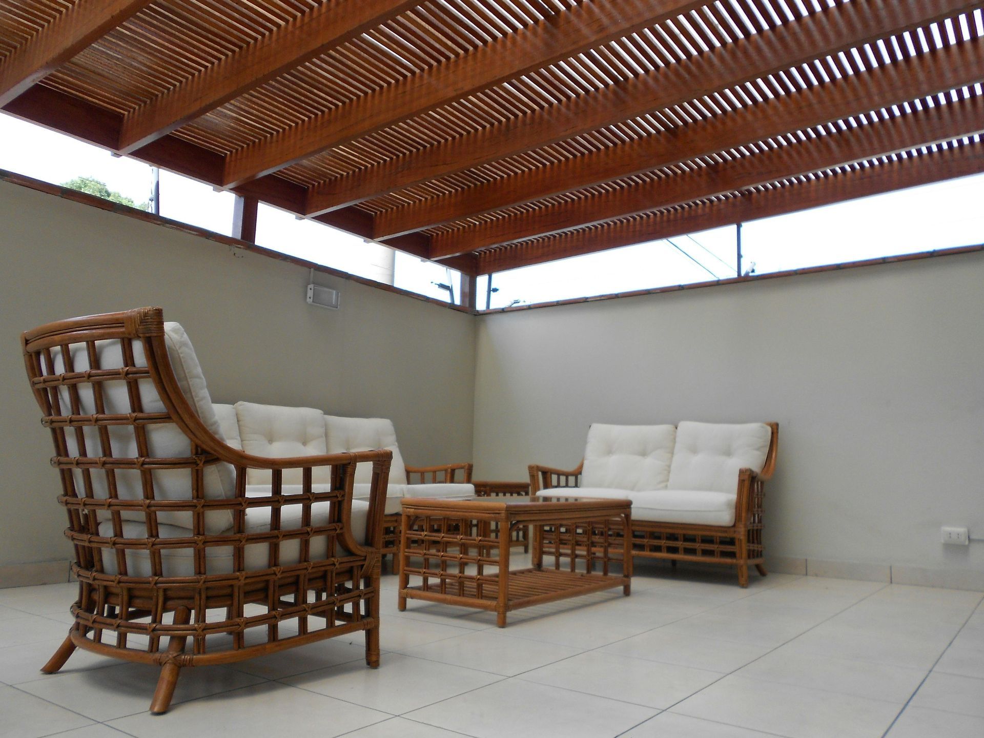 Terrasse avec mobilier en rotin sous un toit à claire-voie en bois.
