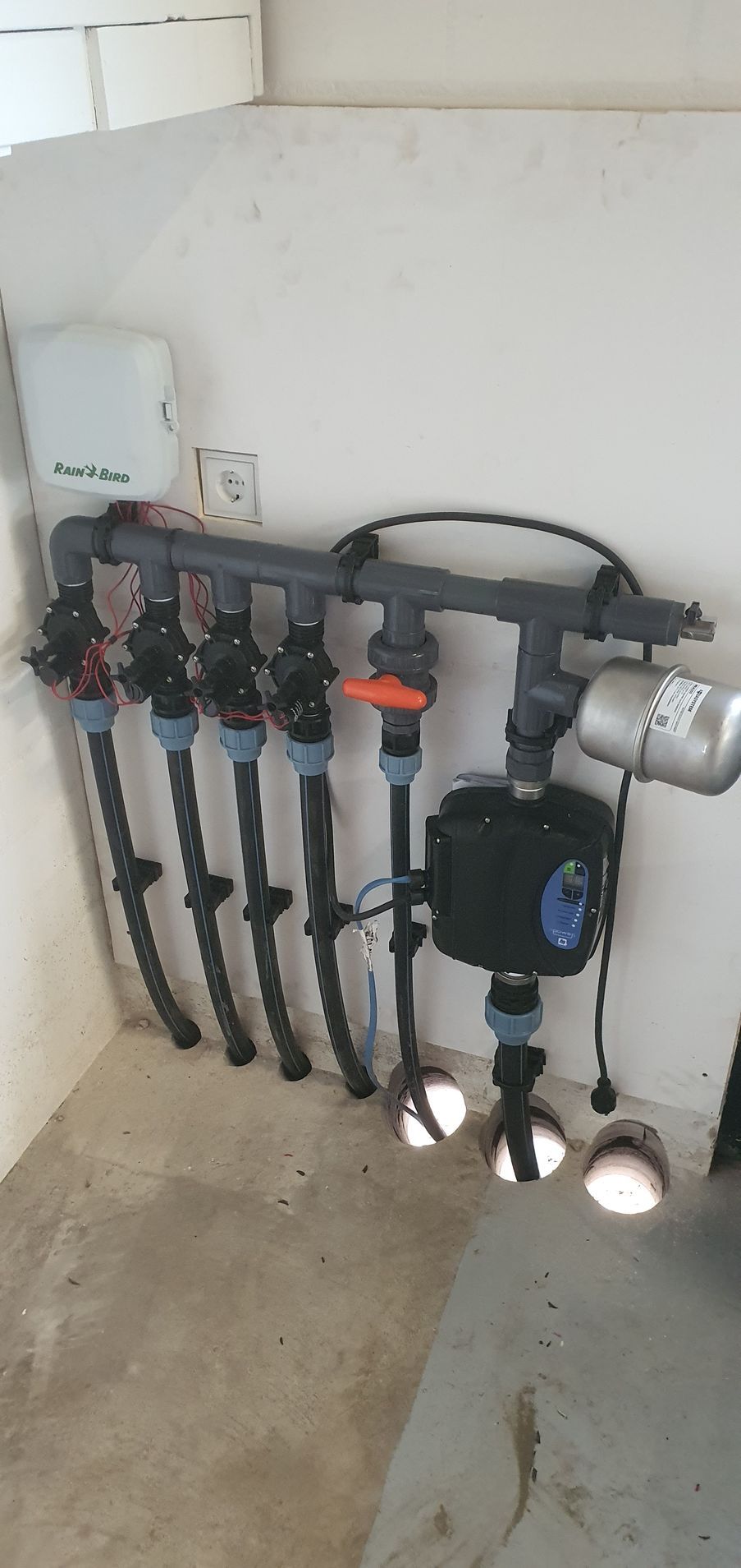 Een irrigatiesysteem met leidingen, afsluiters en een pomp, geïnstalleerd in een hoek van een gebouw.
