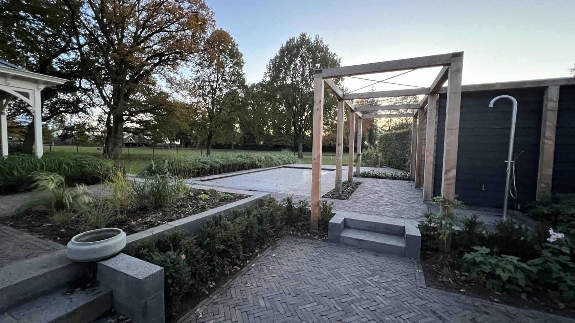 Tuinpad met houten pergola, stenen treden en weelderige beplanting.