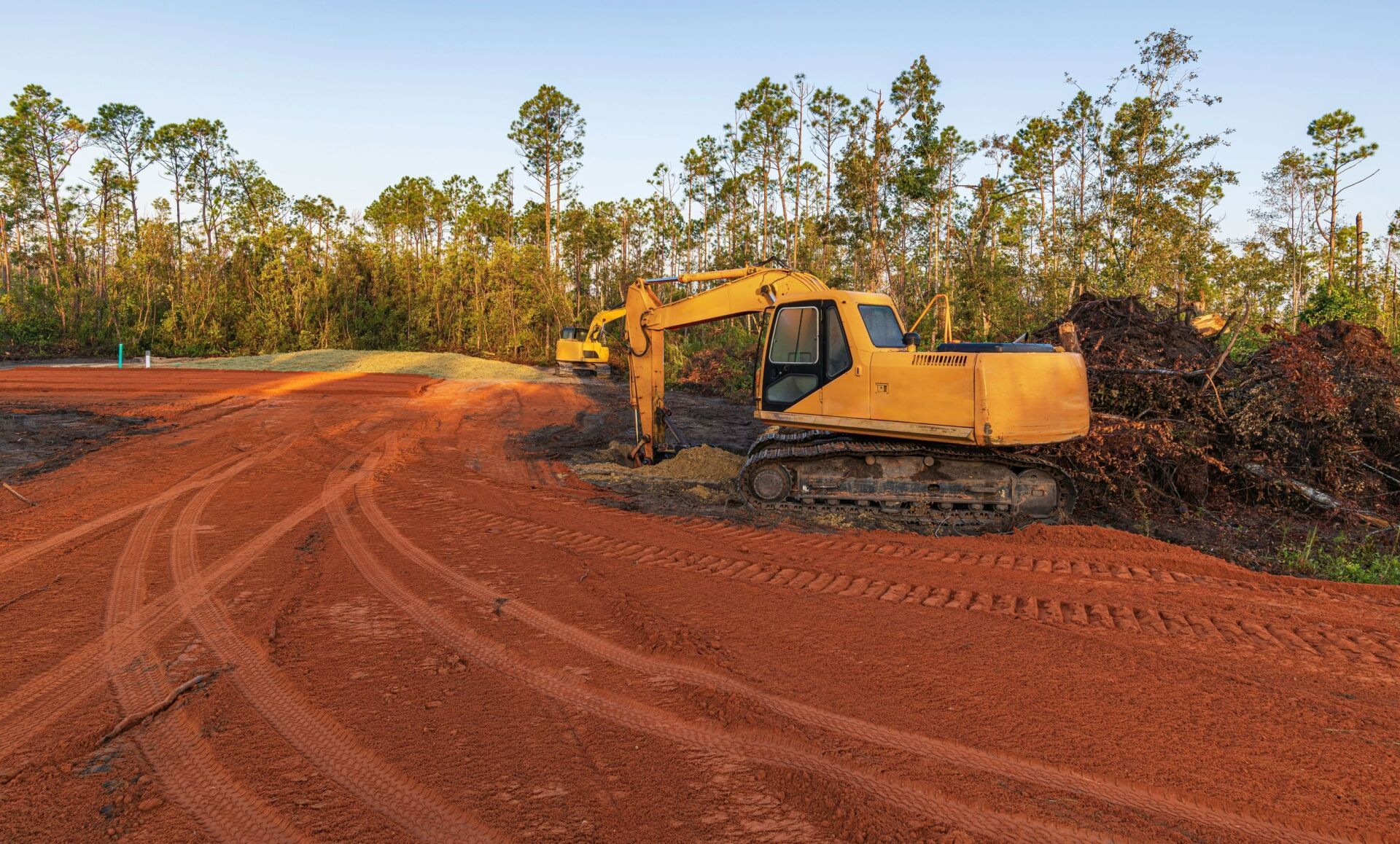 A yellow excavator is working on a dirt road.