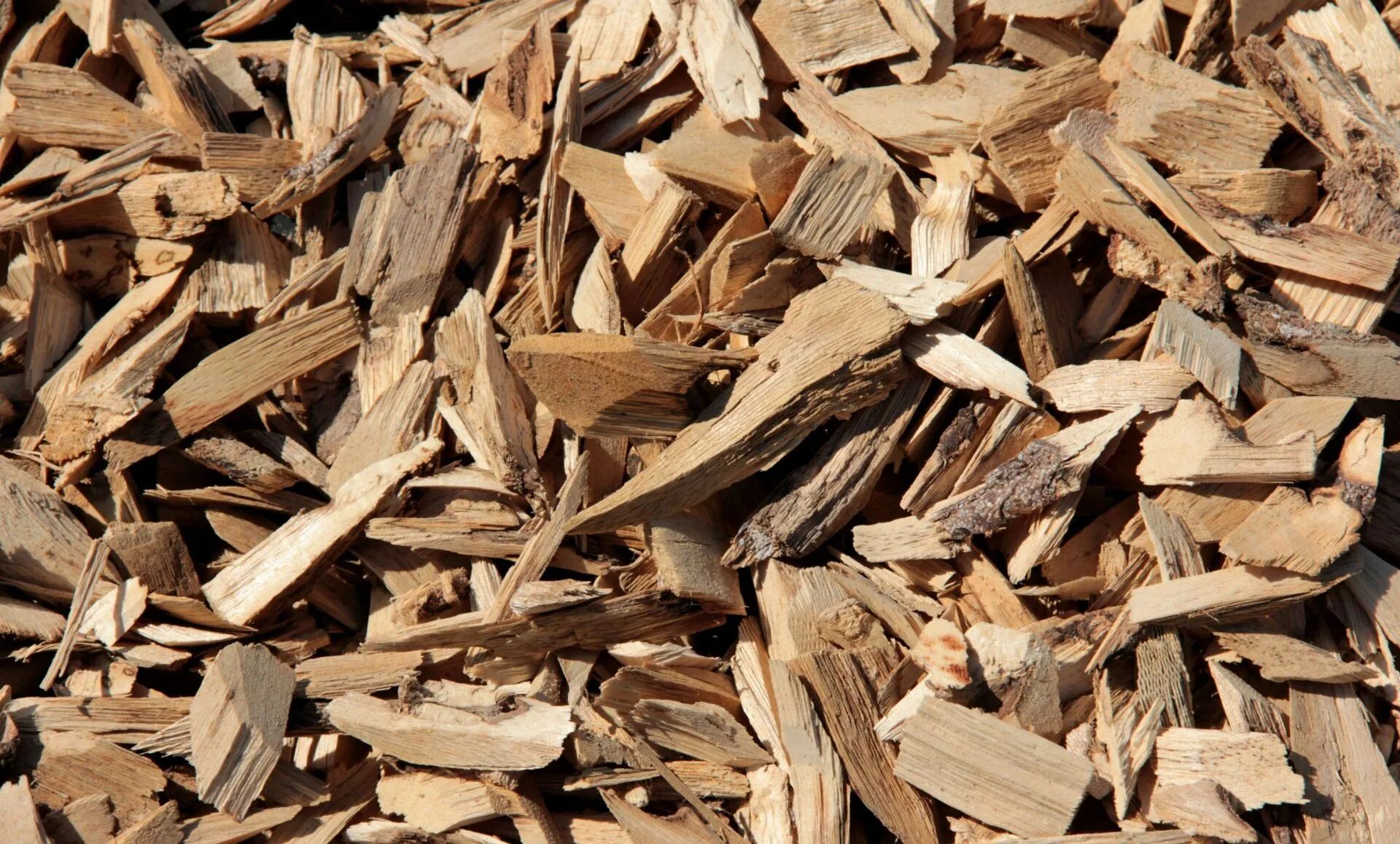 Wood chips, close-up view. Brown, irregular pieces of wood fill the frame, providing ground cover or landscaping material.