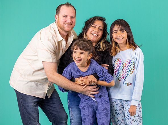 Smiling family of four posing together against a teal background