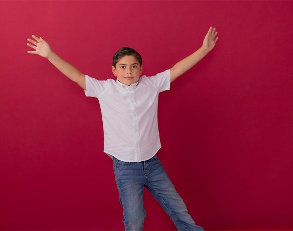 Person posing with arms raised against a bright pink background, wearing a white shirt and jeans.