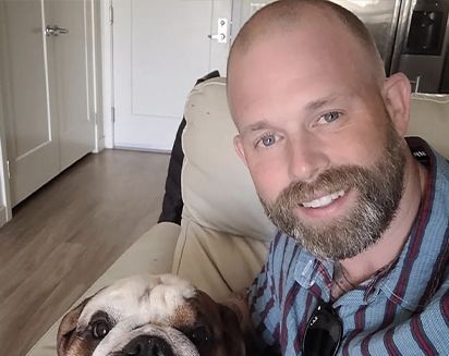 Smiling man and dog on a couch in a bright living room