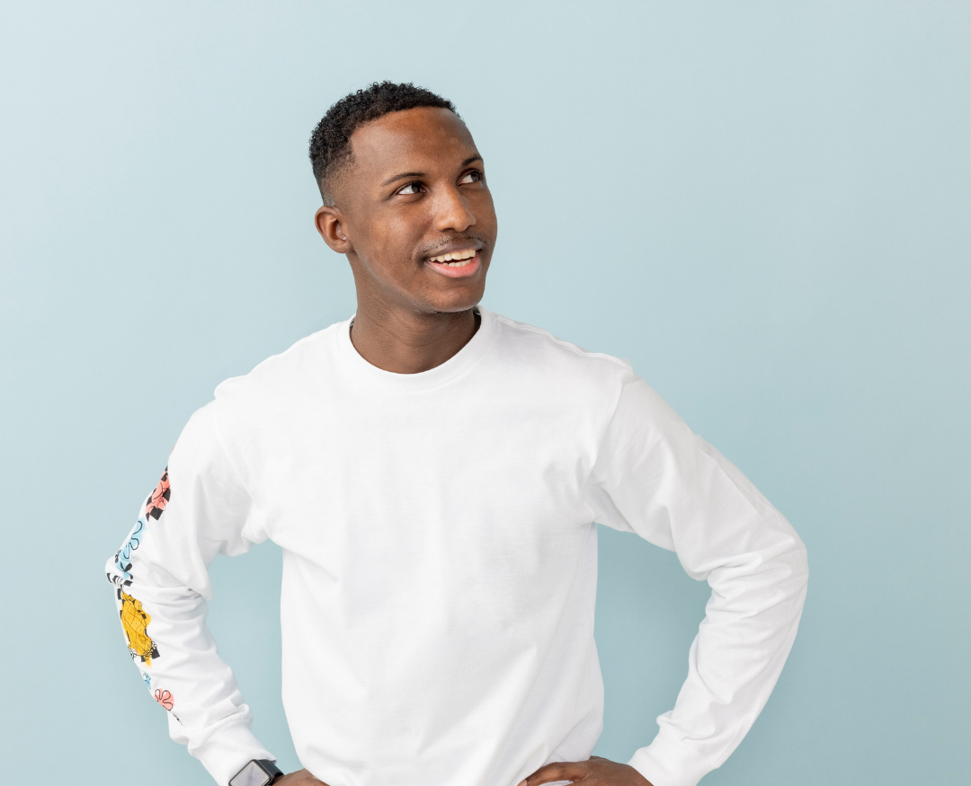Smiling person in a white shirt standing against a light blue background, hands on hips