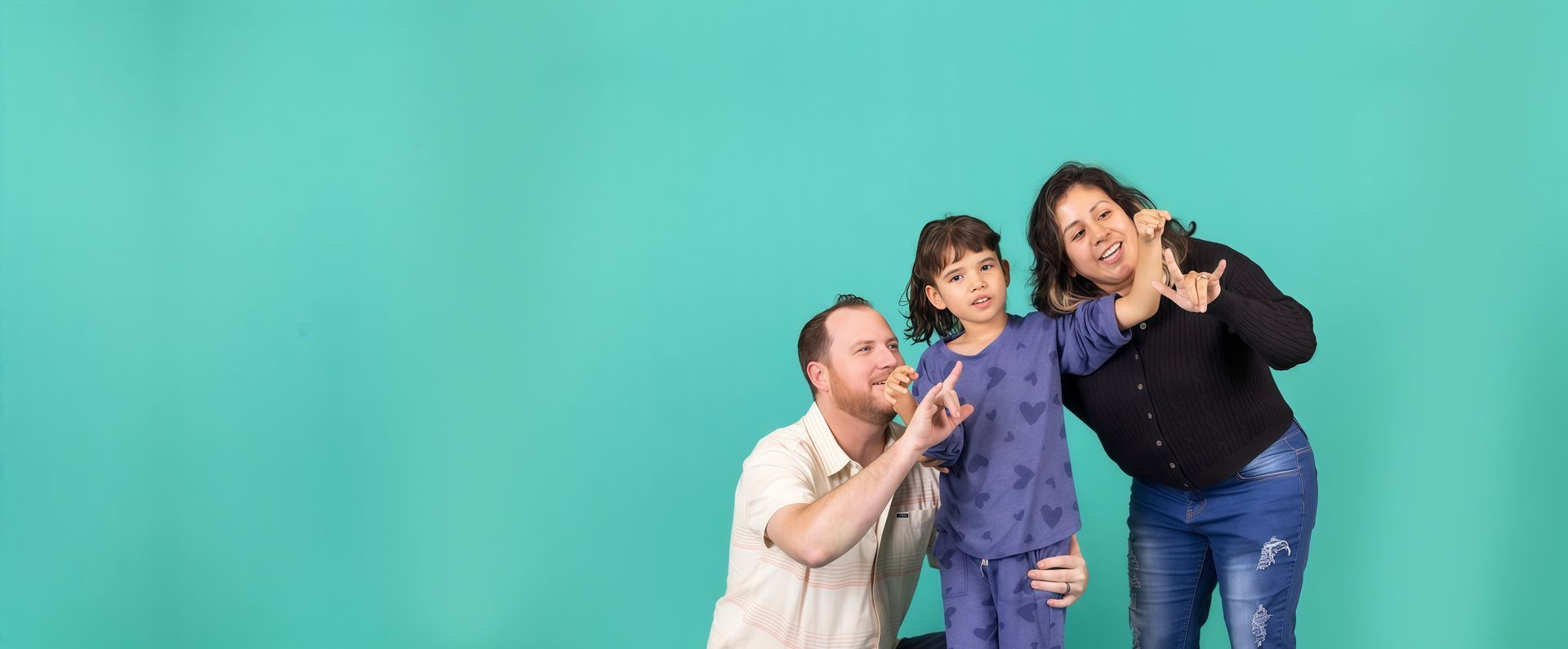 Three people posing playfully against a turquoise background, smiling and gesturing toward the camera