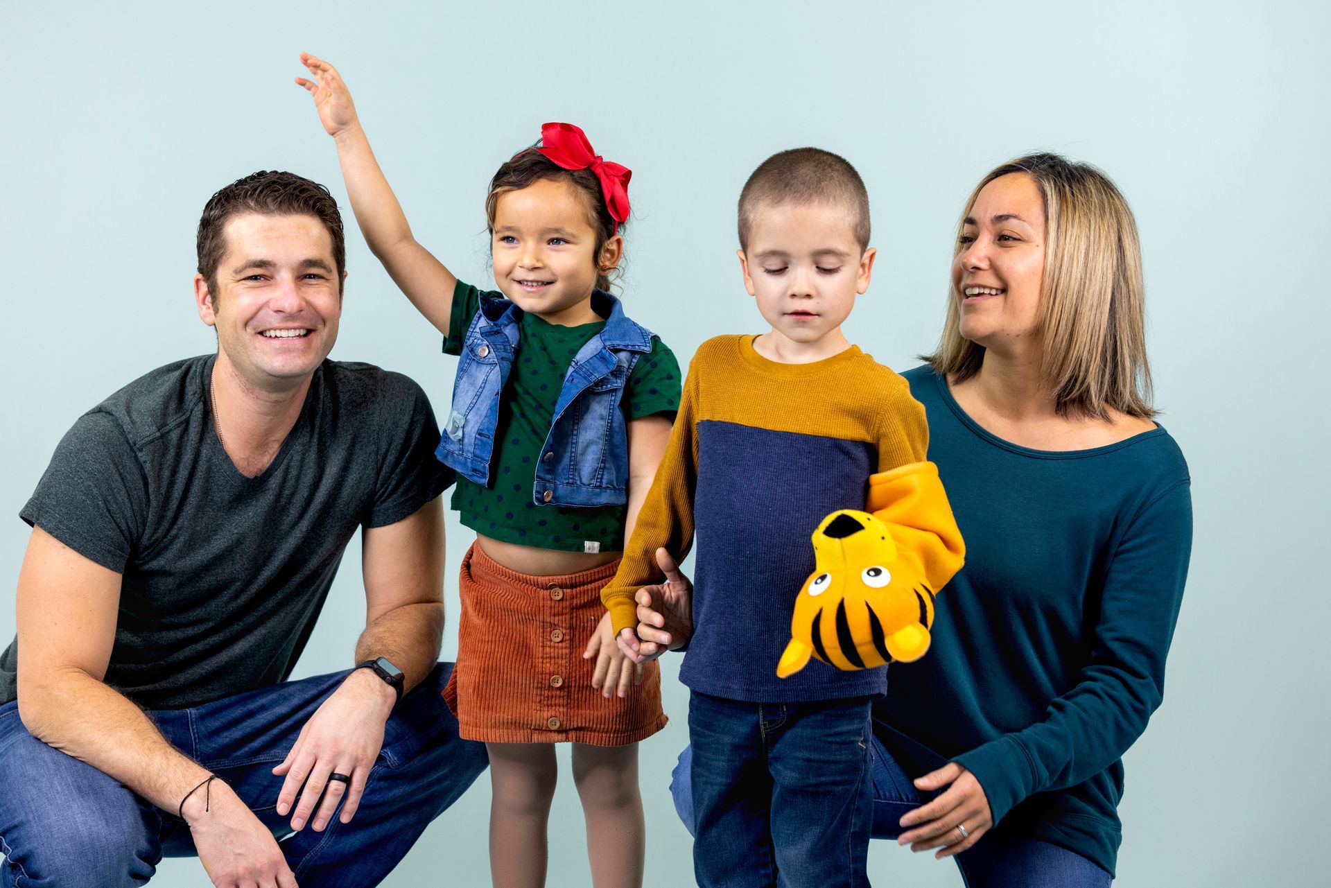 Four people seated against a light background, smiling and posing with a child holding a yellow stuffed toy.