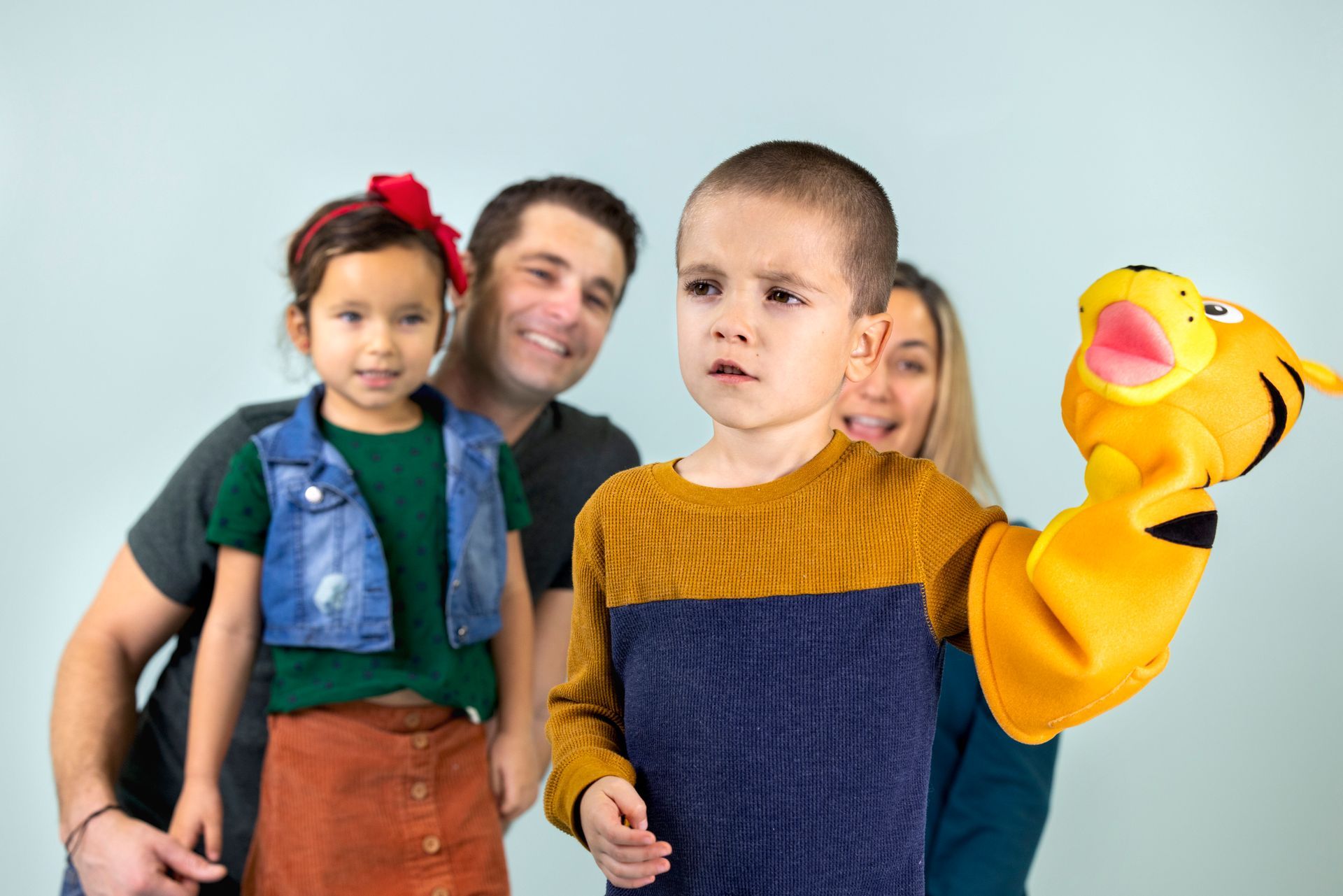 Two children and two adults posing with a yellow puppet on a plain light background