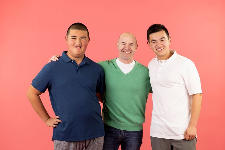 Three people standing together and smiling against a pink background