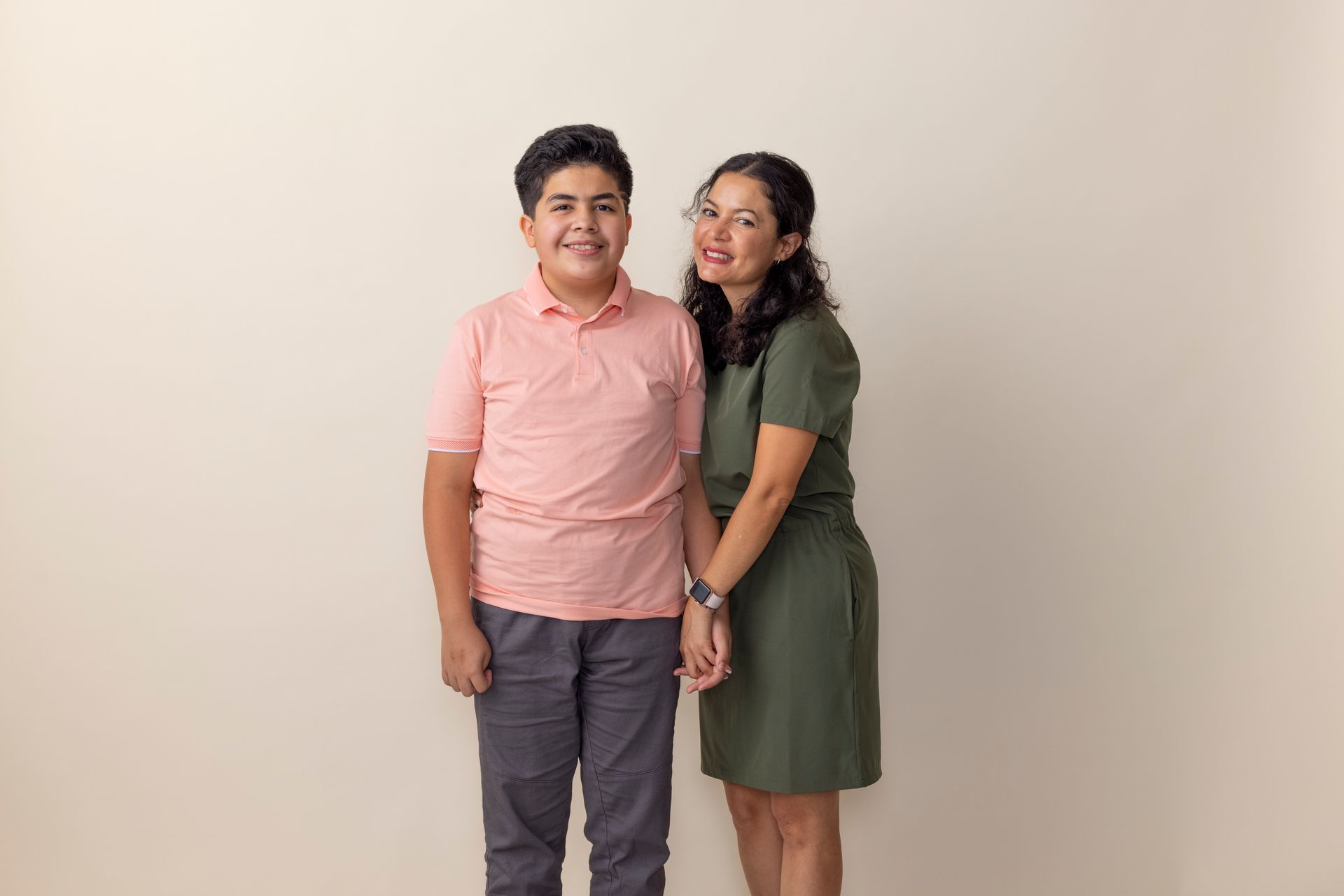 Two people posing together, smiling, against a plain beige wall.