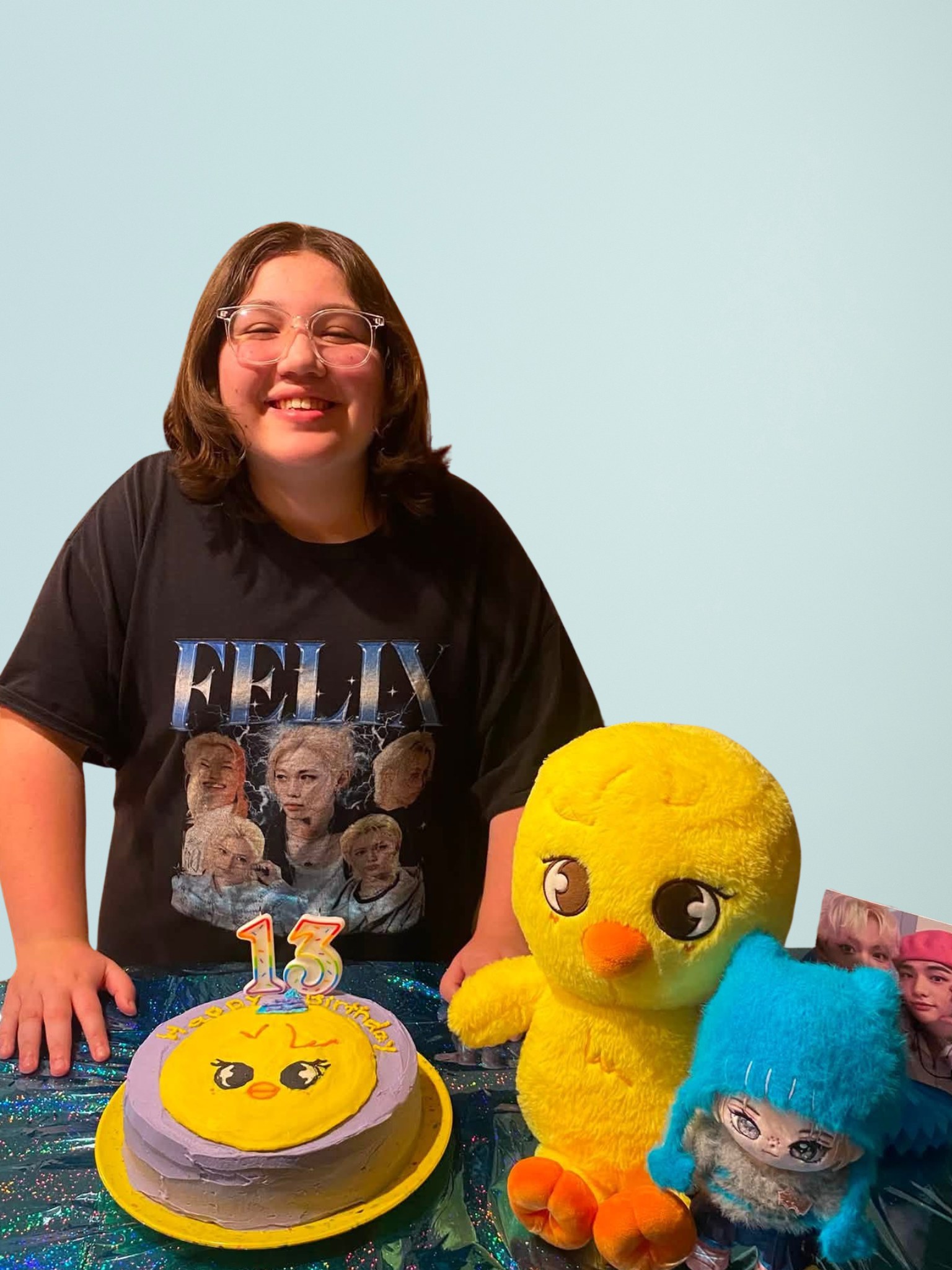 Woman smiling beside a yellow plush duck, blue plush toy, and decorated cake on a table against a light blue wall