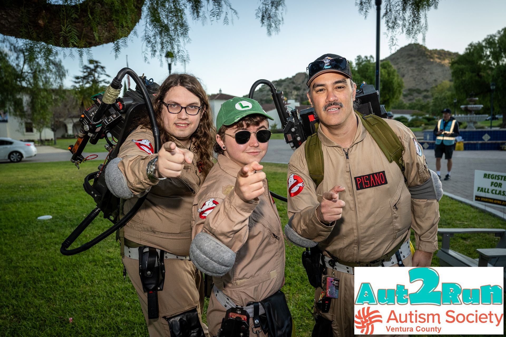 Three people in Ghostbusters-style outfits posing outdoors at an Autism Society event