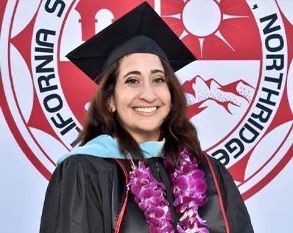 Woman in graduation cap and gown smiling before a California Northbridge seal backdrop